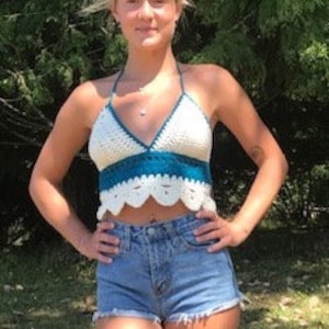 May include: White crochet halter top with a teal and white crocheted trim. The top has a scalloped hem and is worn with denim shorts.