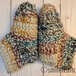 May include: A pair of crocheted slippers in a multi-colored pattern of beige, brown, blue, and yellow. The slippers are made with a chunky yarn and have a textured look.