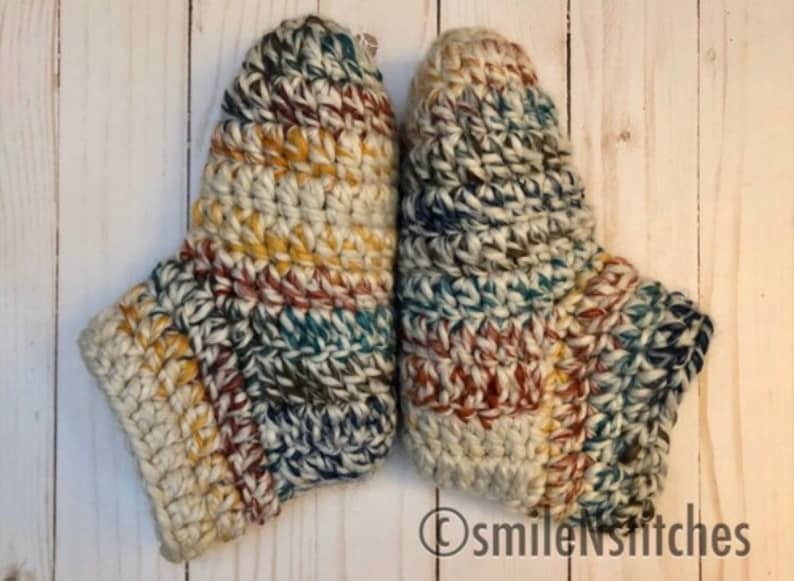 May include: A pair of crocheted slippers in a multi-colored pattern of beige, brown, blue, and yellow. The slippers are made with a chunky yarn and have a textured look.