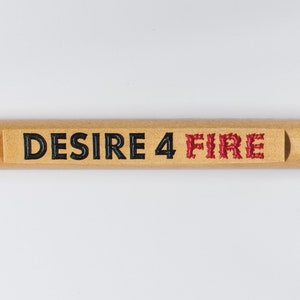 May include: A wooden fire poker with the text "DESIRE 4 FIRE" in black and red. The poker has a light brown handle with a leather loop and a dark metal rod for the poker end. The item is designed for use with a fireplace or campfire.