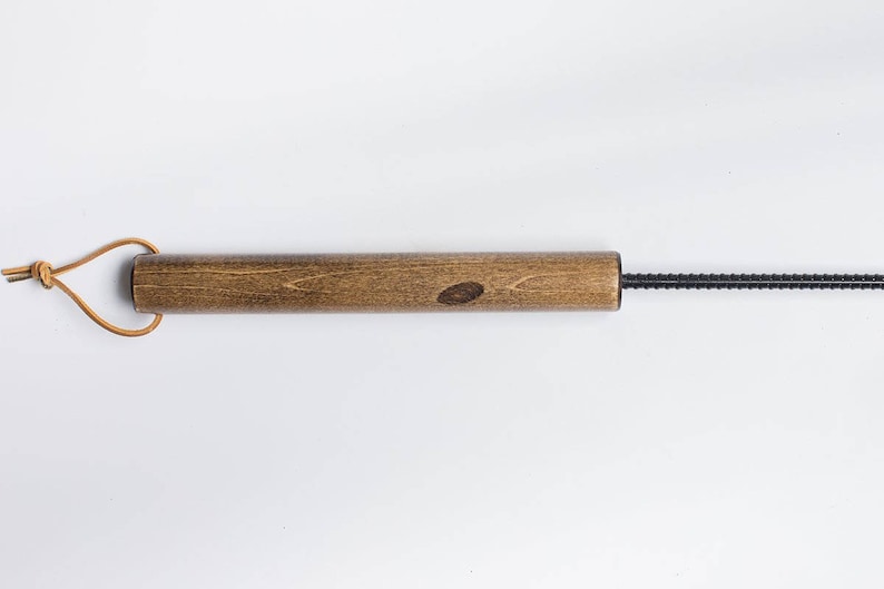 Puede incluir: Una varilla de madera con un alambre de metal negro unido a un extremo. La varilla de madera tiene un lazo de cuero marr&oacute;n unido al otro extremo.