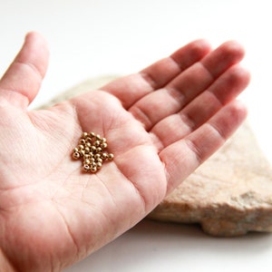 Peut inclure: Un tas de petites perles dorées dans la paume d'une main.