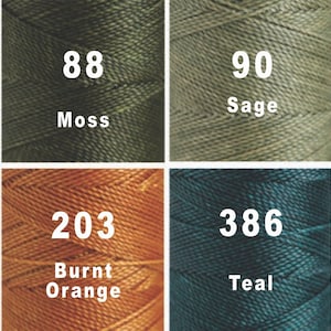 May include: A close-up of eight spools of thread in different colours, including black, moss green, sage green, taupe, blackberry, burnt orange, teal, and black. Each spool has a number and colour name printed on it.