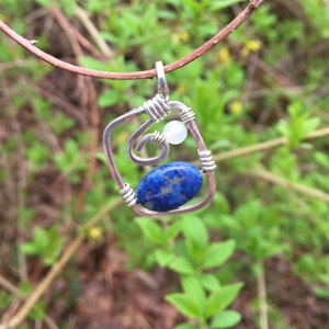 May include: A silver wire wrapped pendant featuring a blue lapis lazuli stone and a white moonstone bead.