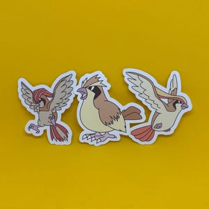 Pode incluir: Três adesivos de pássaros com bordas brancas são exibidos em um fundo amarelo. Os pássaros estão em várias poses, com cores marrom, bege e vermelha. Um pássaro está em pleno voo, outro está cantando e o terceiro está em posição de voo.