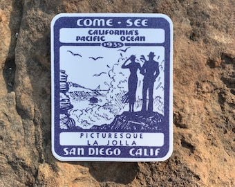 May include: A vintage blue and white sticker with the text "Come See California's Pacific Ocean 1935 Picturesque La Jolla San Diego Calif." and a black and white illustration of a couple looking out at the ocean.
