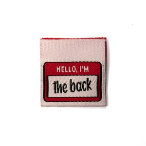 May include: A square, off-white fabric patch with a red border. The patch features a red name tag design with the text "HELLO, I'M" above "the back" in black, sans-serif font. The patch is likely for clothing or accessories.