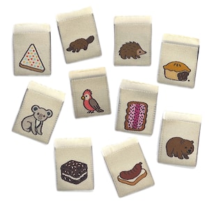 May include: Ten beige fabric patches with embroidered designs. The designs include a pizza slice, a platypus, a hedgehog, a pie, a koala, a bird, a pastry, a bear, a brownie, and a sausage on bread. Each patch has a folded top edge.