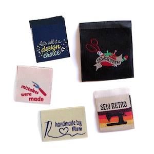 May include: A selection of fabric labels with embroidered text and designs. The labels feature phrases like "let's call it a design choice" and "mistakes were made." Other labels say "handmade by Mum" and "SEW RETRO" with a sewing machine.