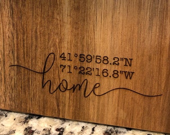 May include: A wooden sign with the word "home" in cursive script and the coordinates "41°59'58.2"N 71°22'16.8"W" engraved on it.