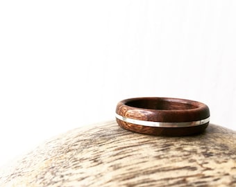 May include: A wooden ring with a silver inlay. The ring is brown and has a smooth finish. It is sitting on a wooden surface.