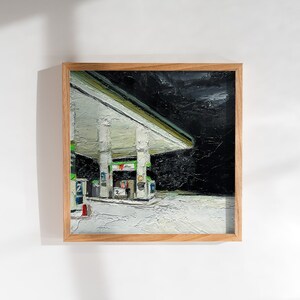 May include: A framed oil painting depicting a petrol station at night. The petrol station is illuminated with white lights and has a green canopy. The sky is dark and overcast.