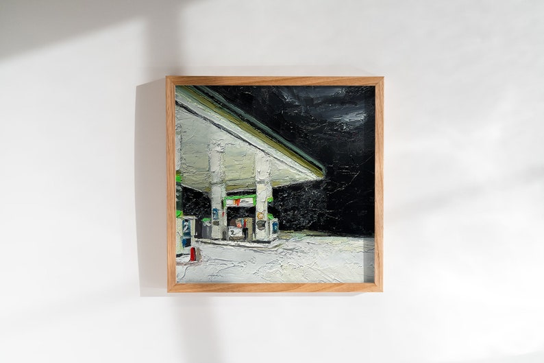 May include: A framed oil painting depicting a petrol station at night. The petrol station is illuminated with white lights and has a green canopy. The sky is dark and overcast.