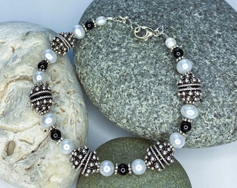 May include: A silver bracelet with white and black beads. The beads are round and have a textured surface. The bracelet has a silver clasp.