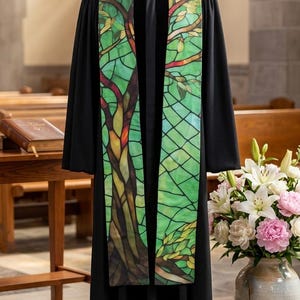 May include: Black clergy robe with a green and multi-colored tree design stole. The stole features a stained-glass effect with a tree trunk and branches. The robe is displayed on a mannequin in a church setting.