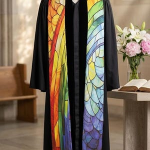 May include: A black clergy robe with a colorful stole. The stole features a stained-glass design with a rainbow of colors, including red, orange, yellow, green, blue, and purple. The robe is displayed on a wooden stand.