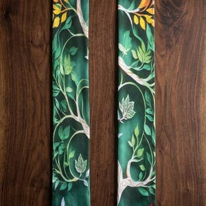 Könnte beinhalten: Ein grünes Stola mit einem Baum- und Regenbogen-Design. Die Stola zeigt eine detaillierte Illustration eines Baumes mit weißen Ästen, grünen Blättern und bunten Schmetterlingen. Am unteren Rand befindet sich ein Regenbogen. Der Hintergrund ist dunkelgrün.
