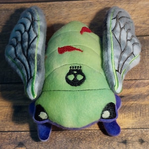 Peluche de cigarra zombi espeluznante y adorable. ¡Una cigarra fuera de lo común! Tiene reflejos que brillan en la oscuridad.