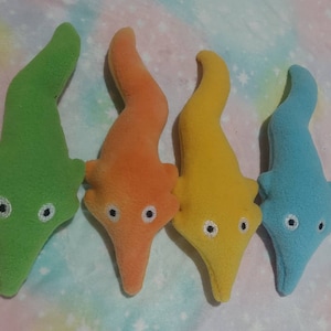 May include: Four plush worm toys in vibrant colors: green, orange, yellow, and blue. Each worm has a curved body, a pointed head, and embroidered eyes. These soft toys are designed for play and display.