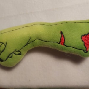 May include: A plush, lime green hand with black embroidered outlines and red embroidered wounds. The hand is in a grasping position, with the fingers slightly curled. The design is reminiscent of a zombie or monster hand, perfect for Halloween or horror-themed decor.