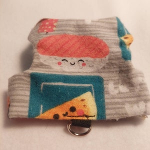 Può includere: Un'imbracatura per animali domestici in tessuto grigio con un design a tema sushi. L'imbracatura presenta un personaggio di sushi sorridente, una fetta di pizza e altre grafiche a tema cibo. Ha un cinturino nero e un anello di metallo argentato.