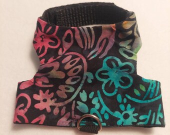 May include: A small pet harness with a black base fabric and a colorful floral pattern in pink, teal, and yellow. The harness has a black nylon neck strap and a silver metal D-ring for leash attachment.