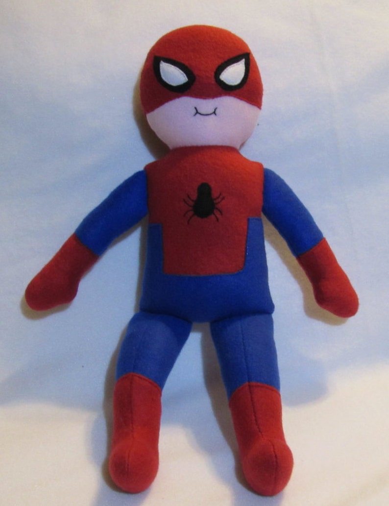 May include: A red and blue plush toy of Spiderman with a white face and black eyes. The toy has a spider symbol on the chest.
