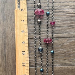 May include: A silver chain necklace with pink and blue faceted glass beads. The necklace is approximately 15 inches long.