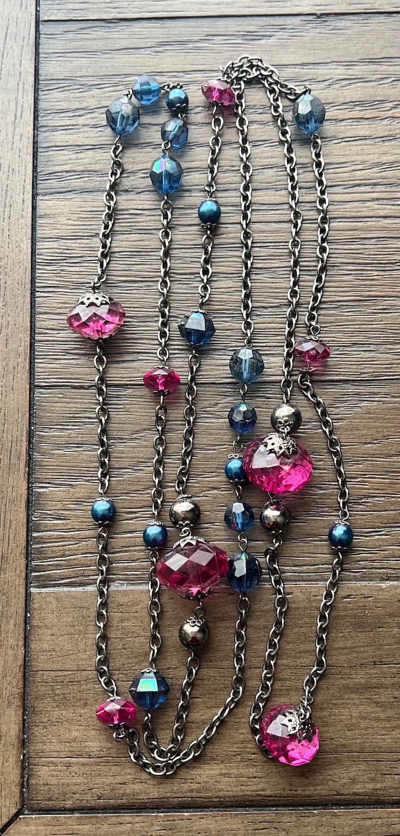 May include: A silver chain necklace with pink and blue faceted glass beads. The necklace has a layered look with multiple strands of chain.