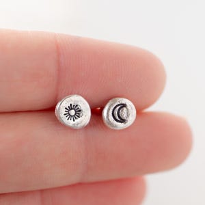 May include: A pair of silver stud earrings with a sun and moon design. The earrings are small and delicate, and they would make a great gift for someone who loves celestial jewelry.