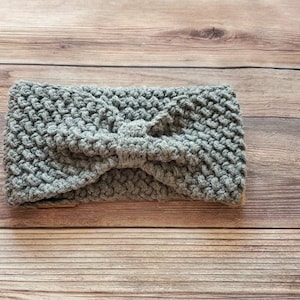 May include: Gray knitted headband with a knotted bow detail. The headband is made of a soft, textured yarn.