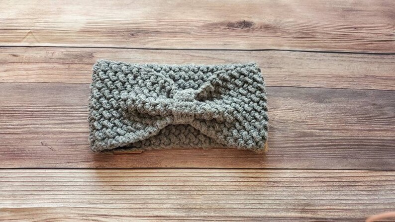 May include: Gray knitted headband with a knotted bow detail. The headband is made of a soft, textured yarn.