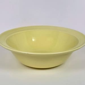 May include: A pale yellow ceramic bowl with a wide, flat rim and a smooth, glossy finish. The bowl features a deep, rounded basin and a consistent, solid light yellow color throughout its entire surface, presenting a simple, functional design.