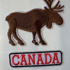 Peut inclure: Ensemble de patchs brodés. Un patch représente un orignal brun avec une bordure blanche. Le second patch est rectangulaire, avec le mot "CANADA" en lettres rouges sur fond blanc et bordure noire. Coutures détaillées.