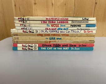 May include: A stack of vintage children's books with colorful covers. Titles include "The Cat in the Hat" and "Green Eggs and Ham" by Dr. Seuss, and others. The books are stacked on a light gray surface.