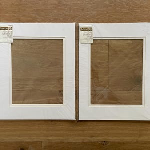 May include: Two white double beveled mats for picture frames, each featuring a rectangular cutout and a label in the top left corner that reads home double beveled mat 8 inch by 10 inch opening for 11 inch by 14 inch frame.