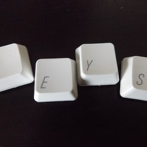 May include: Four white computer keyboard keys spelling the word "KEYS". The keys are arranged on a dark surface. The letters are in a simple sans-serif font.