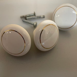 Peut inclure: Boutons de meuble en céramique blanche avec une bordure dorée. Les boutons sont de forme ovale et sont livrés avec des vis argentées. Ces boutons décoratifs peuvent être utilisés pour moderniser l'aspect des meubles.