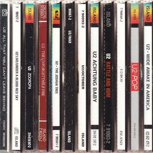 May include: A collection of U2 music CDs, featuring album titles like "Achtung Baby," "The Joshua Tree," and "Zooropa." The spines display album art and the Island Records logo. The CDs are in their original jewel cases, with a variety of colors and designs.