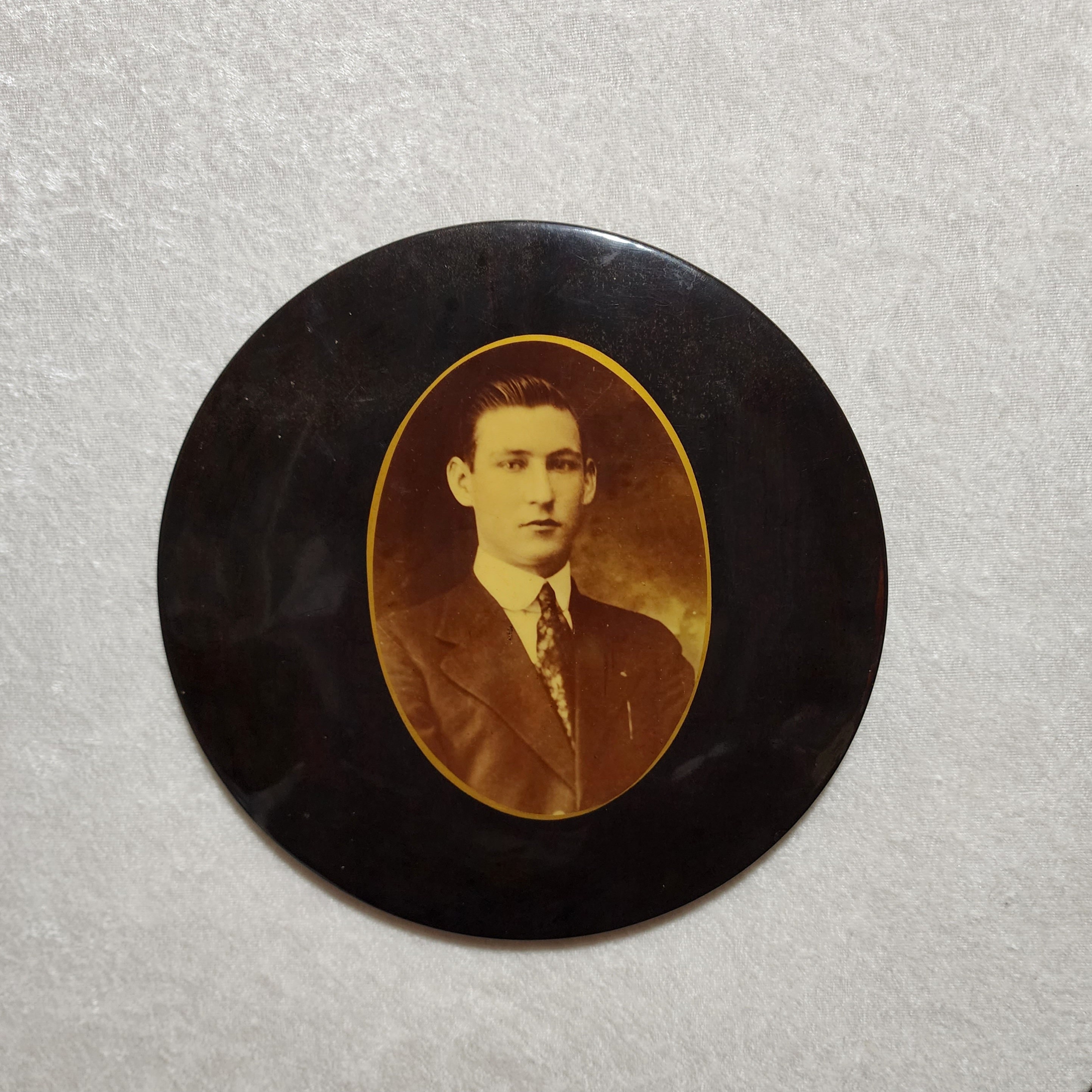 A celluloid tin photo button. An all black mourning portrait of a young  man. Antique. 1900s.