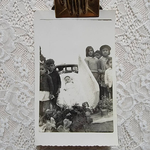 Vintage black and white snapshot of children standing next to their deceased sibling. September 1952. Post mortem child in a casket. Texas.