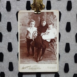 Une belle photo de carte de cabinet de l'ère victorienne de 3 frères et sœurs assis sur une chaise en osier. Fille aînée en tenue de deuil noire. Stryker, Ohio