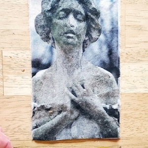 以下が含まれることがあります： 古典的な彫像のグレースケール画像が描かれた長方形の布パッチ。胸の前で手を組んだ姿が描かれています。パッチの長さは約10cmです。