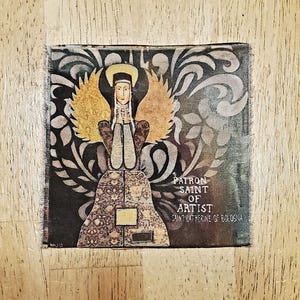 May include: A vintage-style patch featuring a woman in a brown dress with a halo, surrounded by gold and black floral designs. The text reads "Patron Saint of Artist Saint Catherine of Bologna".