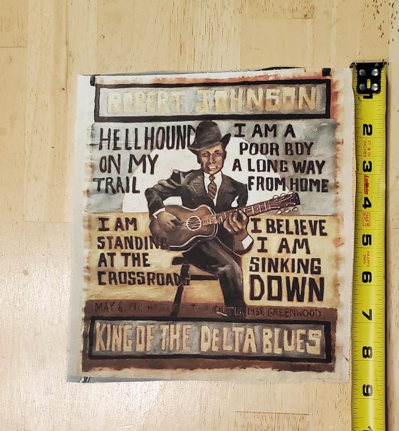 Pu&ograve; includere: Stampa quadrata con un dipinto di Robert Johnson che suona la chitarra. La stampa include il testo che recita "Hellhound on my trail" e "King of the Delta Blues". La stampa &egrave; alta circa 15 cm.