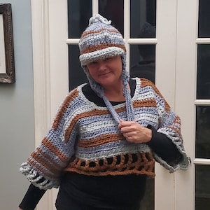 May include: A crocheted top with brown and blue stripes and a matching crocheted hat with a pom-pom on top. The hat has ear flaps that tie under the chin.