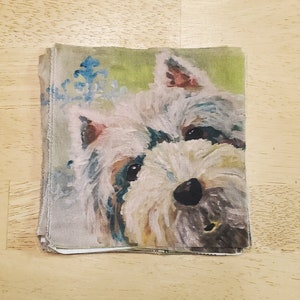 May include: Close-up of a white dog with brown ears and a black nose. The dog is painted on a fabric with a green background and blue floral accents.