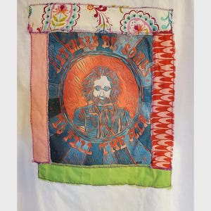 May include: A white t-shirt with a colorful patchwork design featuring a portrait of a man with long hair and sunglasses. The text "There By Some To Fill The Air" is printed on the patch.