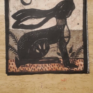 May include: Black and white illustration of a rabbit with a crescent moon in the background. The rabbit is sitting on a patterned surface with leaves and branches.