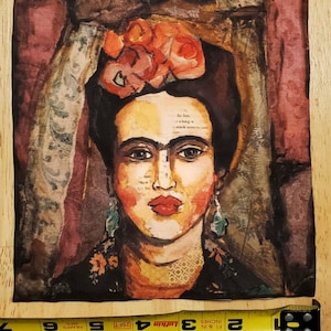 May include: A colorful painting of Frida Kahlo with a flower crown and a unibrow. The painting is on a fabric background with a floral pattern.